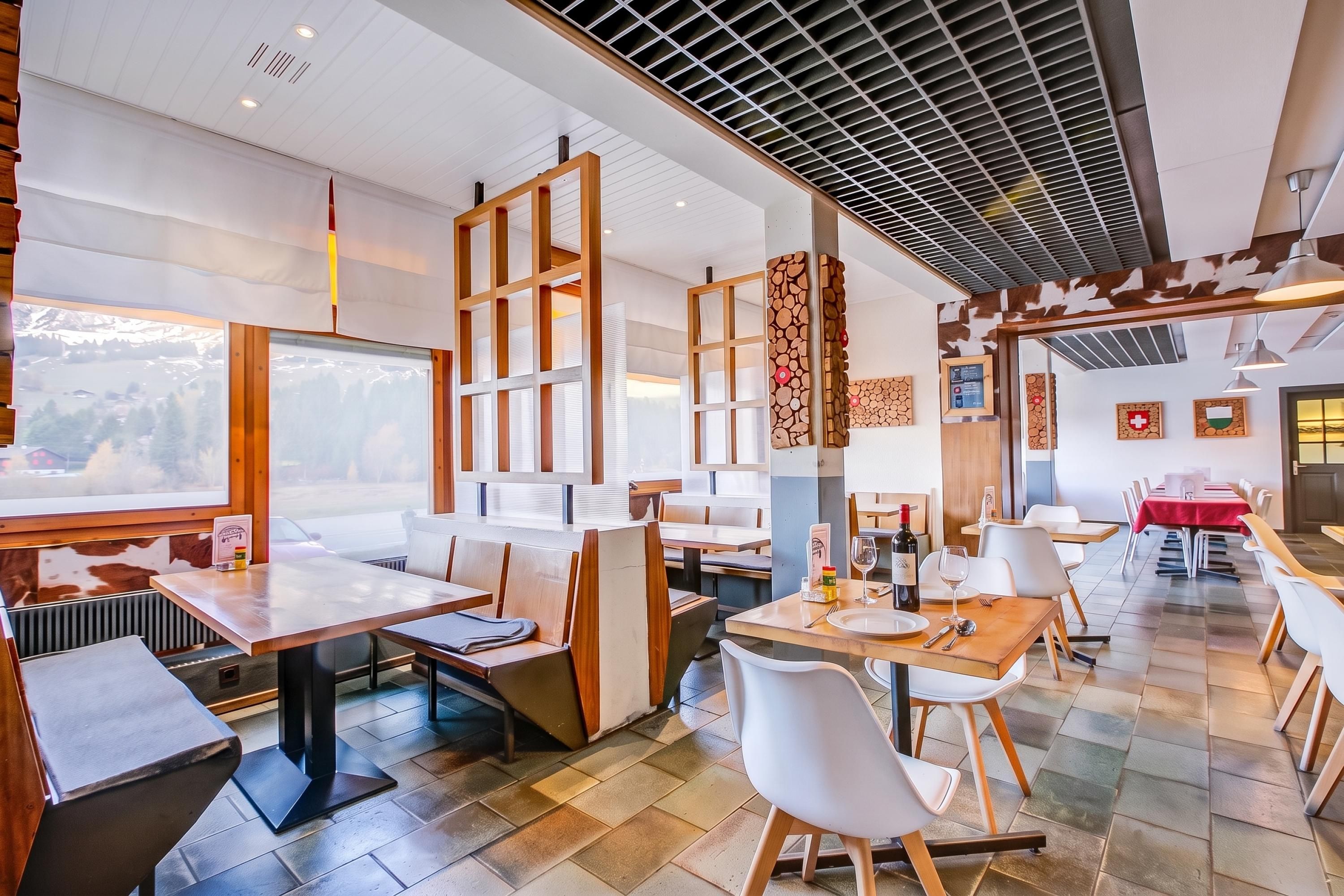 A restaurant with multiple dining areas, including a booth section and a table section. There are wooden chairs and tables, and the ceiling features a grid-like pattern.