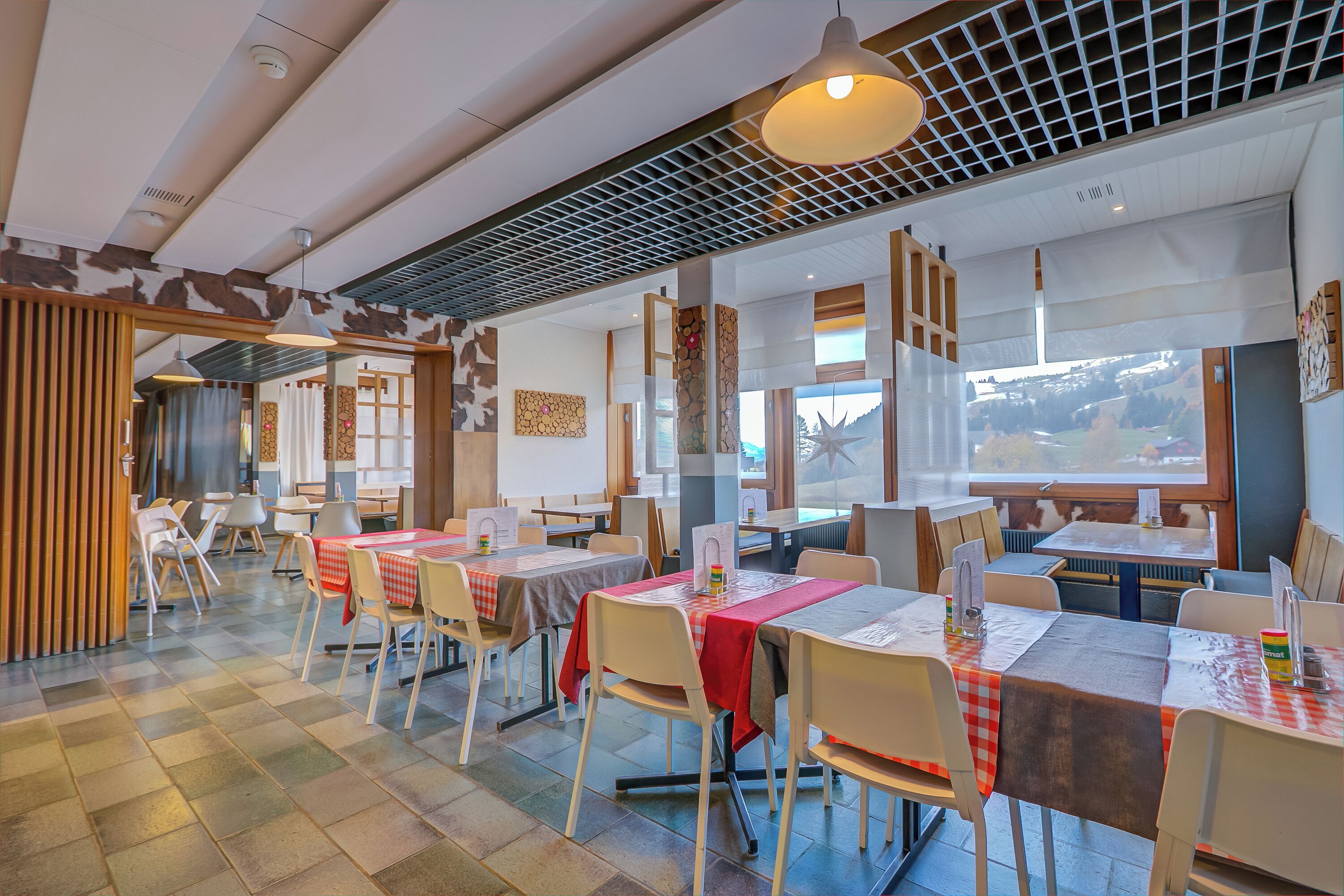 Un restaurant doté de nombreuses tables et chaises, d’un sol carrel é et offrant une vue sur l’extérieur.