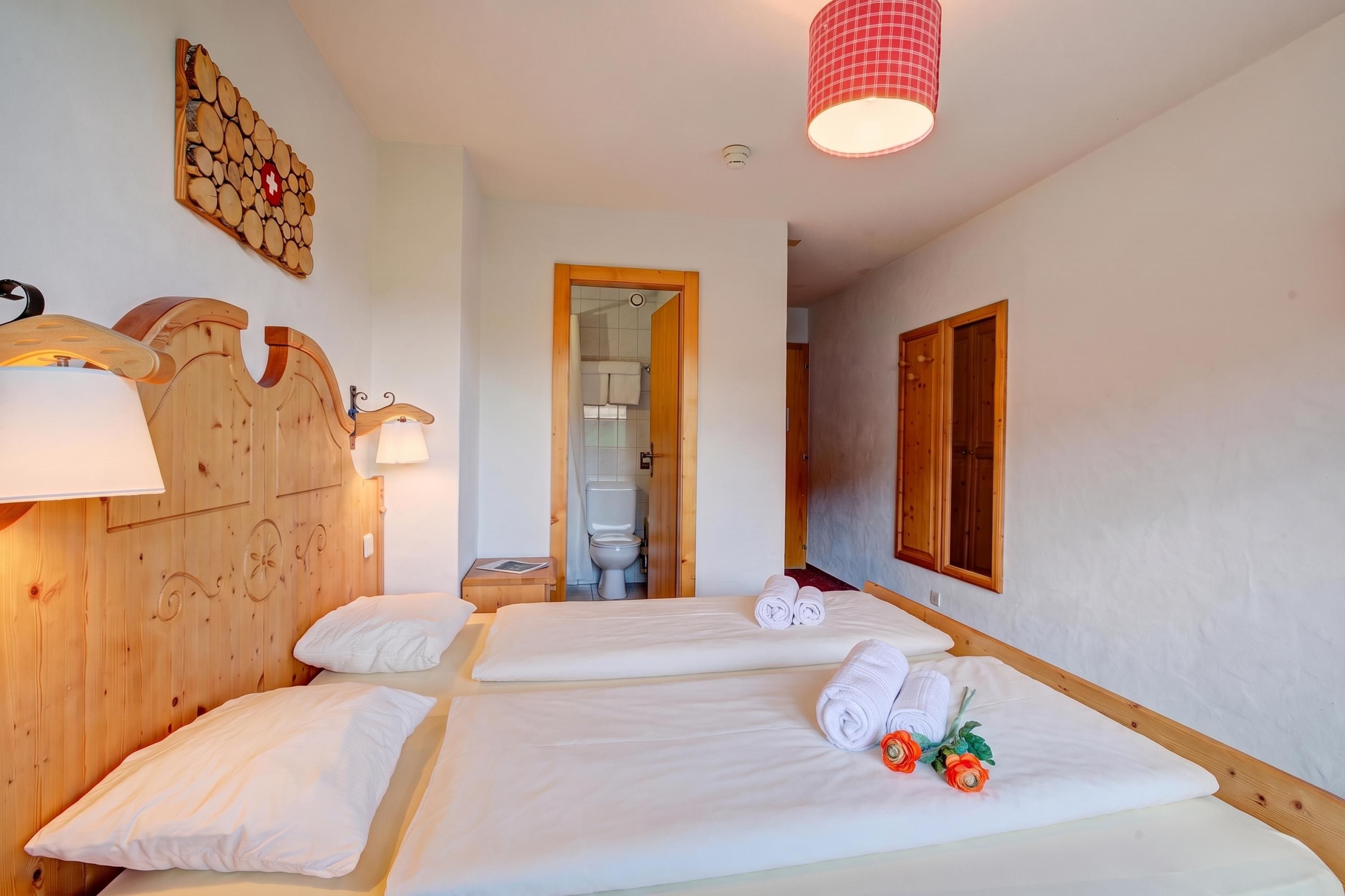 A hotel room with two beds, a wooden headboard, a wall-mounted lamp, and a bathroom visible through an open door.