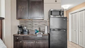 Una cocina compacta con alacenas de madera oscura, un refrigerador de acero inoxidable, un microondas y una cafetera.