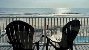 Un balcón con dos sillas Adirondack que da a una playa con vista despejada al océano.