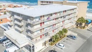 Un hotel de varios pisos con balcones, estacionamiento y vista al océano.