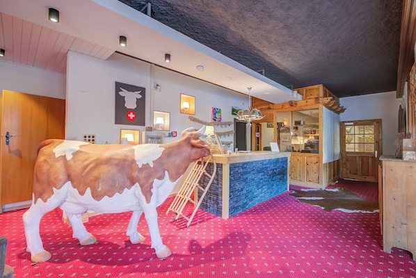 A room with a cow statue, a wooden bar, and a red patterned floor. - Hotel Relais Alpin Twin Room & Balcony5 233, Les Mosses, Switzerland (Les Mosses)