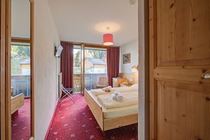 Ein Schlafzimmer mit einem hölzernen Bett, einem roten Teppich, einem Sessel, einem Schreibtisch und Blick durch eine Glastür.