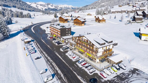 Un pueblo cubierto de nieve con edificios, una carretera serpenteante y coches aparcados.