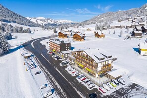 Vila coberta de neve com edifícios, uma estrada sinuosa e carros estacionados.