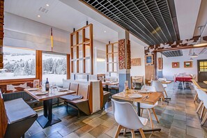 Un restaurant au décor moderne, avec des meubles en bois et une vue sur des montagnes enneigées.