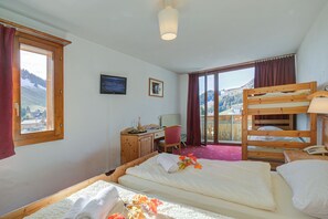 Une chambre avec un lit superposé, un bureau avec une chaise, un lit avec une serviette roulée et une fenêtre avec des rideaux.