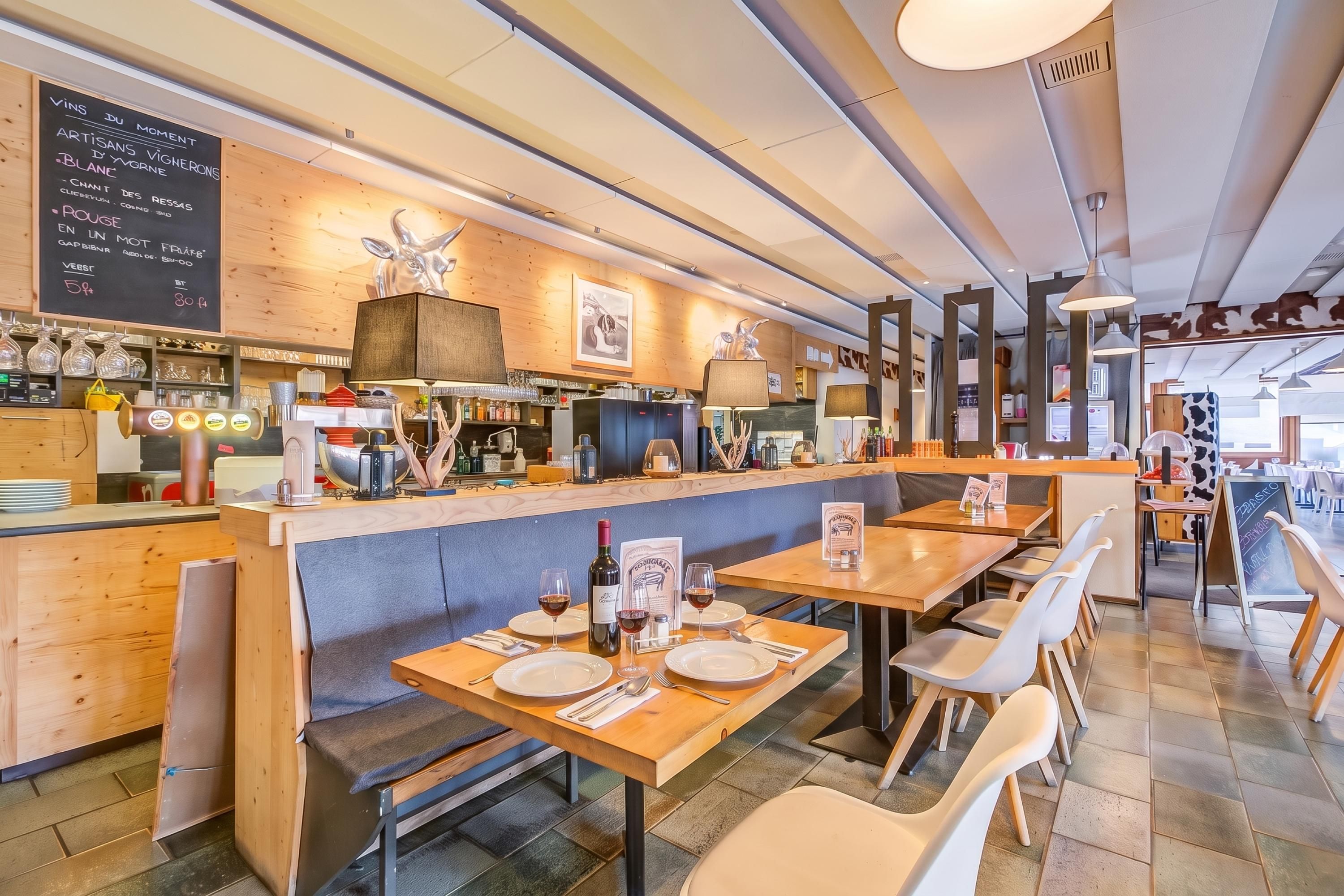 Ein Restaurantinnenraum mit Holztischen und -bänken, einer Bar und einer Tafel mit der Speisekarte.