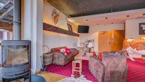 Een gezellige woonkamer met een open haard, comfortabele zitplaatsen, een televisie en een decoratief hertenhoofd aan de muur.