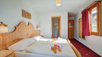 Ein Hotelzimmer mit zwei Holzbett, einem hölzernen Kopfteil, einem Nachttisch aus Holz und einer Wandlampe. Ein Fenster mit rotem Vorhang.