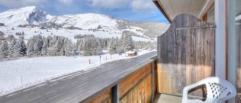 A balcony with a view of a snowy mountain landscape, a wooden railing, and a white plastic chair.