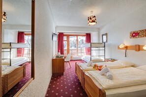 Habitación de hotel con dos camas, un escritorio, una silla, un espejo y un ventanal con cortinas rojas.