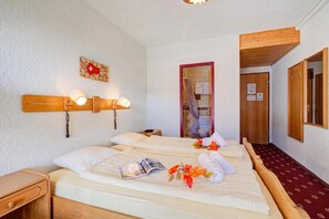Una habitación de hotel con cama, mesitas de noche, cabecera de madera, lámpara fijada a la pared y una puerta que da al baño.