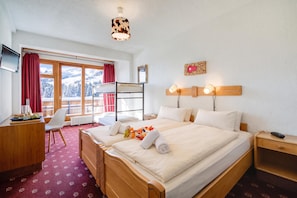 Habitación de hotel con cama, escritorio, silla, televisor y ventana con vista a montañas nevadas.