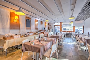 Un restaurante con varias mesas, iluminación colgante y vistas al exterior.