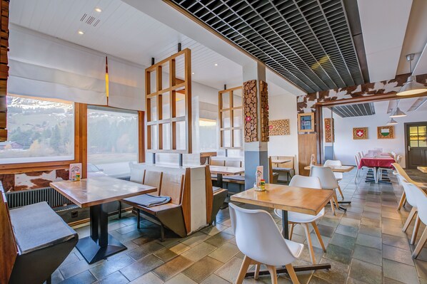 Ein Restaurant mit hohen Tischen, Sitzecken und großen Fenstern mit Blick, sowie einem modernen Deckenstil.
