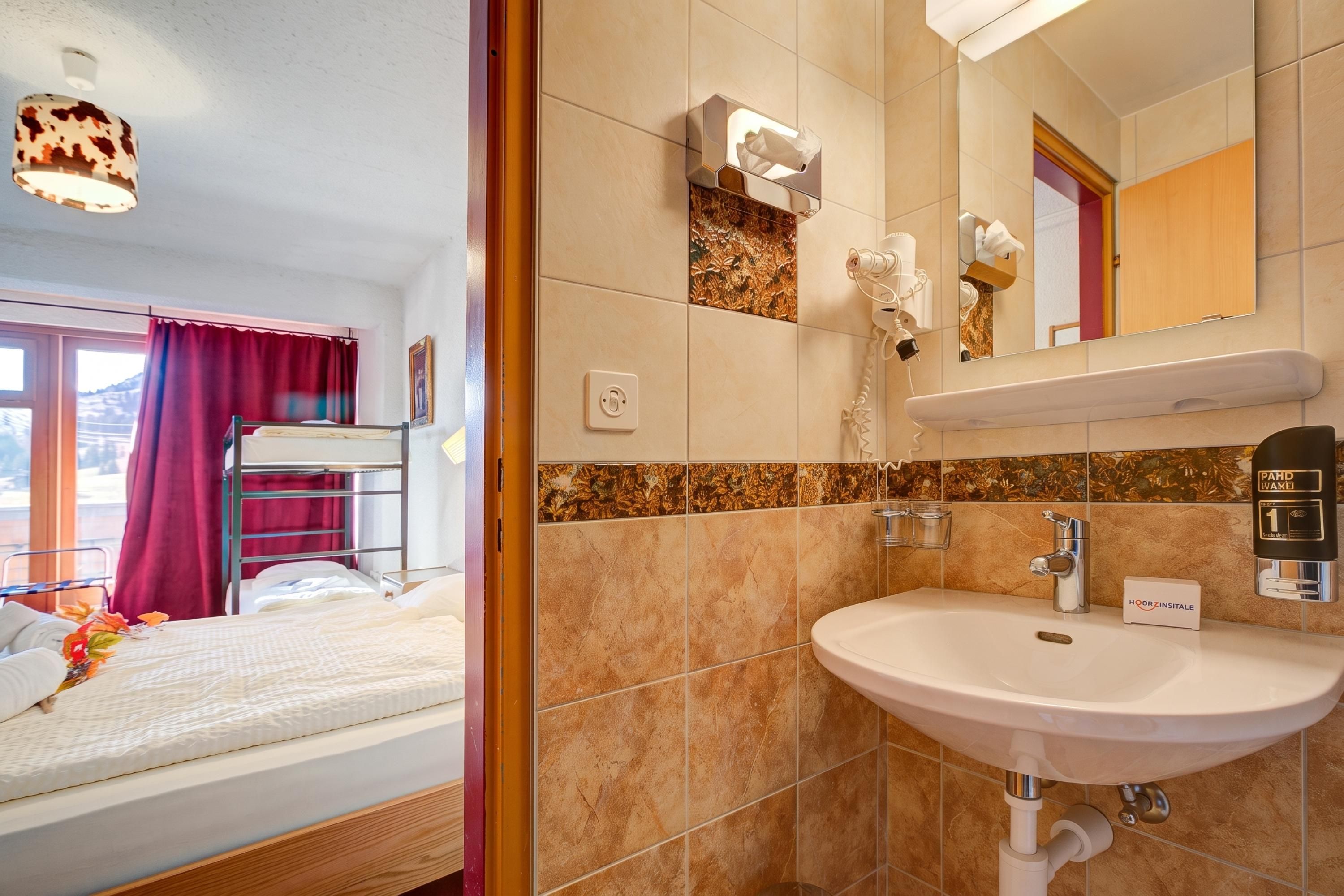 A hotel room with a bunk bed, a bathroom with a sink, a mirror, and a towel dispenser.