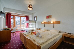 Habitación de hotel con cama, escritorio, silla, ventana con vista a un paisaje nevado y una lámpara de pared.