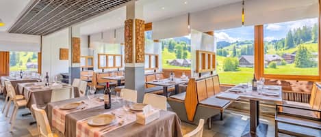 Een restaurant met meerdere eettafels, stoelen en uitzicht op een groen landschap door grote ramen.