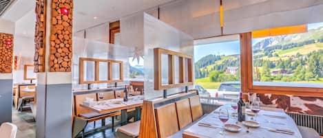 A restaurant with wooden wall decor, tables set for dining, and a view of a mountainous landscape.