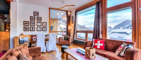 A cozy living room with a fireplace, a sofa, a coffee table, and a large window with a mountain view.