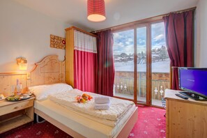 Ein Hotelzimmer mit Bett, Fernseher, einem Holz-Kopfteil, einem Nachttisch mit Flasche und Gläsern sowie einem Fenster mit Vorhängen.
