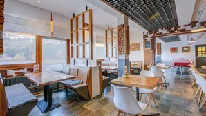 A restaurant with high tables and booths, large windows with a view, and a modern ceiling design.