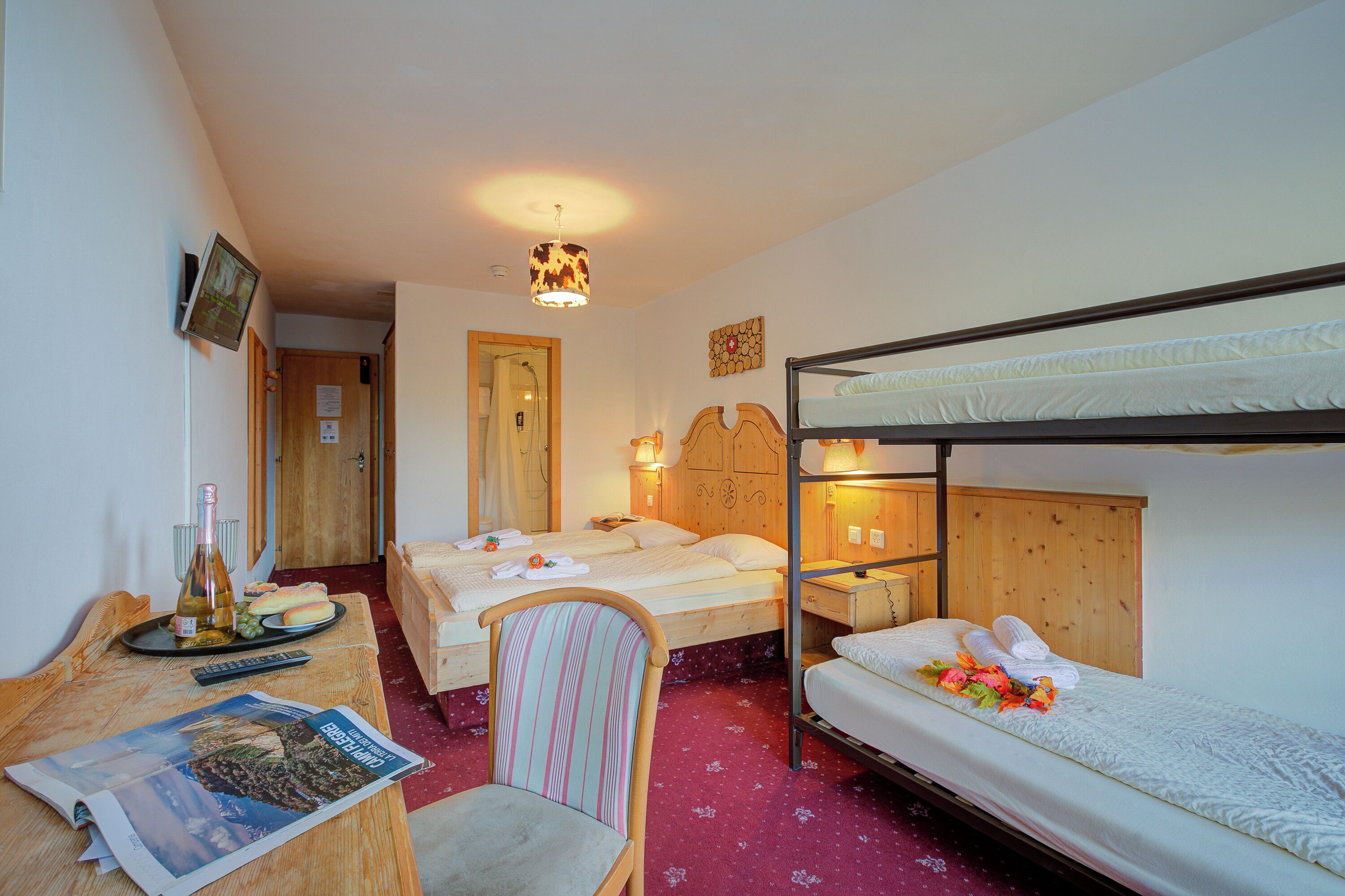 A hotel room with bunk beds, a desk with a newspaper, a chair, a wooden table, and a lamp.