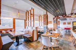 Een restaurant met verschillende eetgedeeltes, waaronder een gedeelte met zitbanken en een gedeelte met tafels. Er zijn houten stoelen en tafels, en het plafond heeft een rasterpatroon.