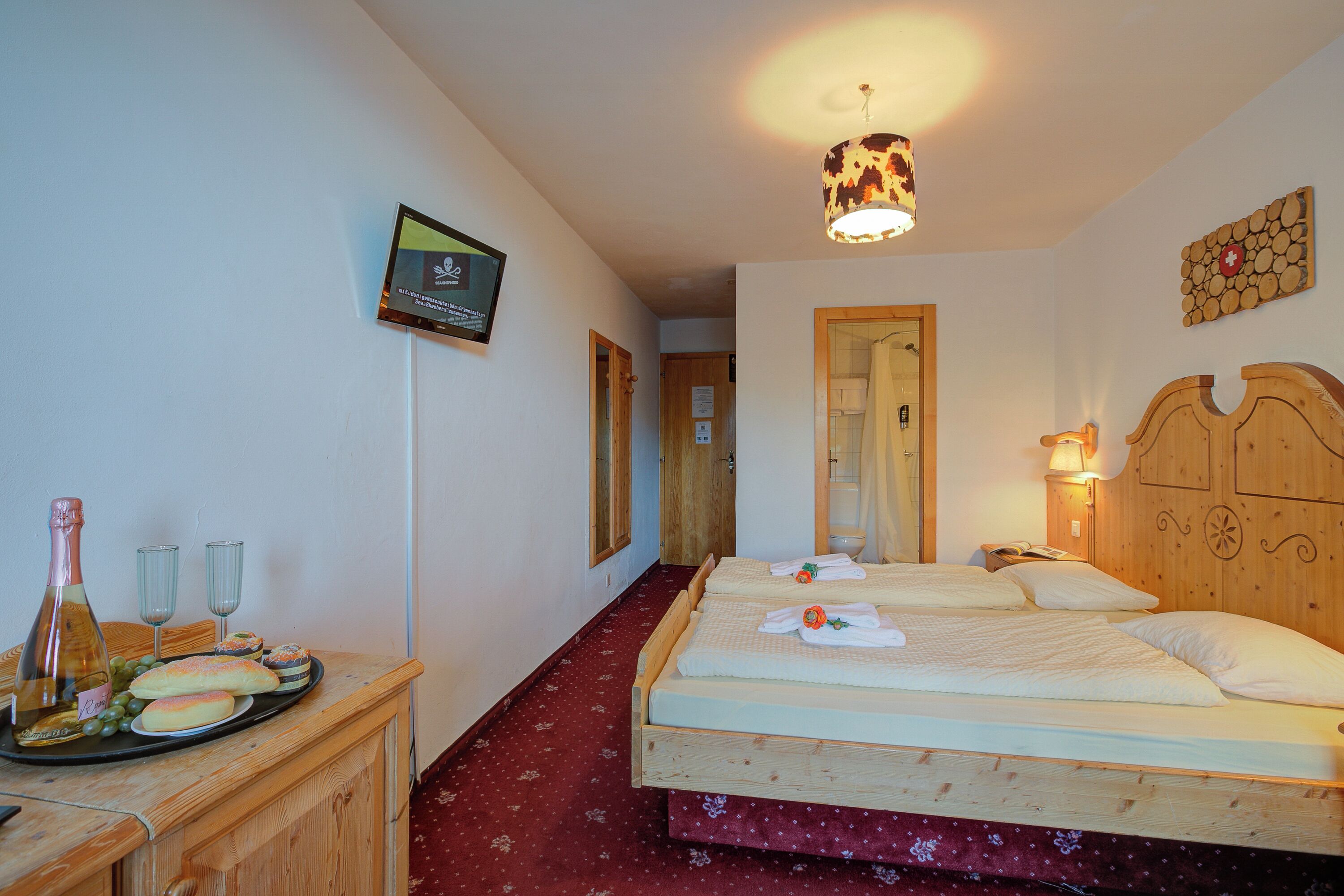 Habitación de hotel con dos camas, cabecera de madera, armario de madera, televisor y alfombra roja.