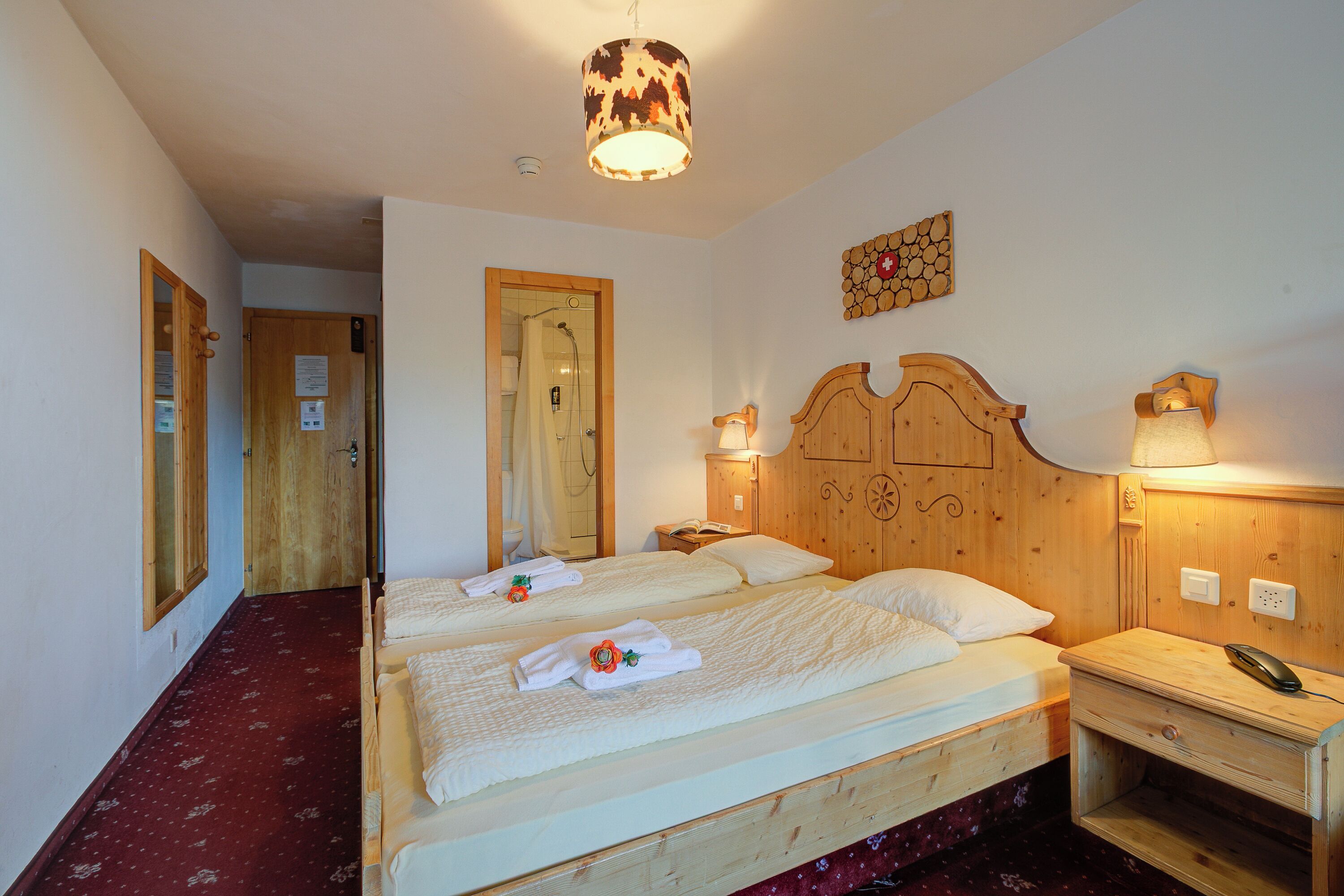 Una habitación con dos camas, cabeceros de madera, una mesita de noche de madera con un teléfono y una lámpara de pared.
