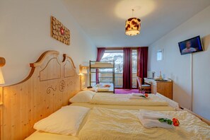 Habitación de hotel con dos camas, cabecera de madera, televisión y vista a un paisaje nevado.