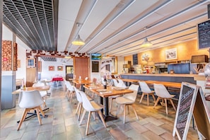 Interior moderno de restaurante con mesas y sillas de madera, una zona de bar y un panel con la carta.