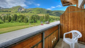 Ein Balkon mit Blick auf eine Straße, grüne Hügel und ein kleines Gebäude.