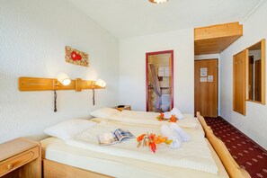 Habitación de hotel con dos camas, cabecero de madera, mesita de noche, lámpara de pared y puerta de madera con espejo.