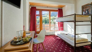Una habitación con literas, una mesa de comedor con una bandeja de comida y bebidas, una silla y una ventana con vistas a montañas.