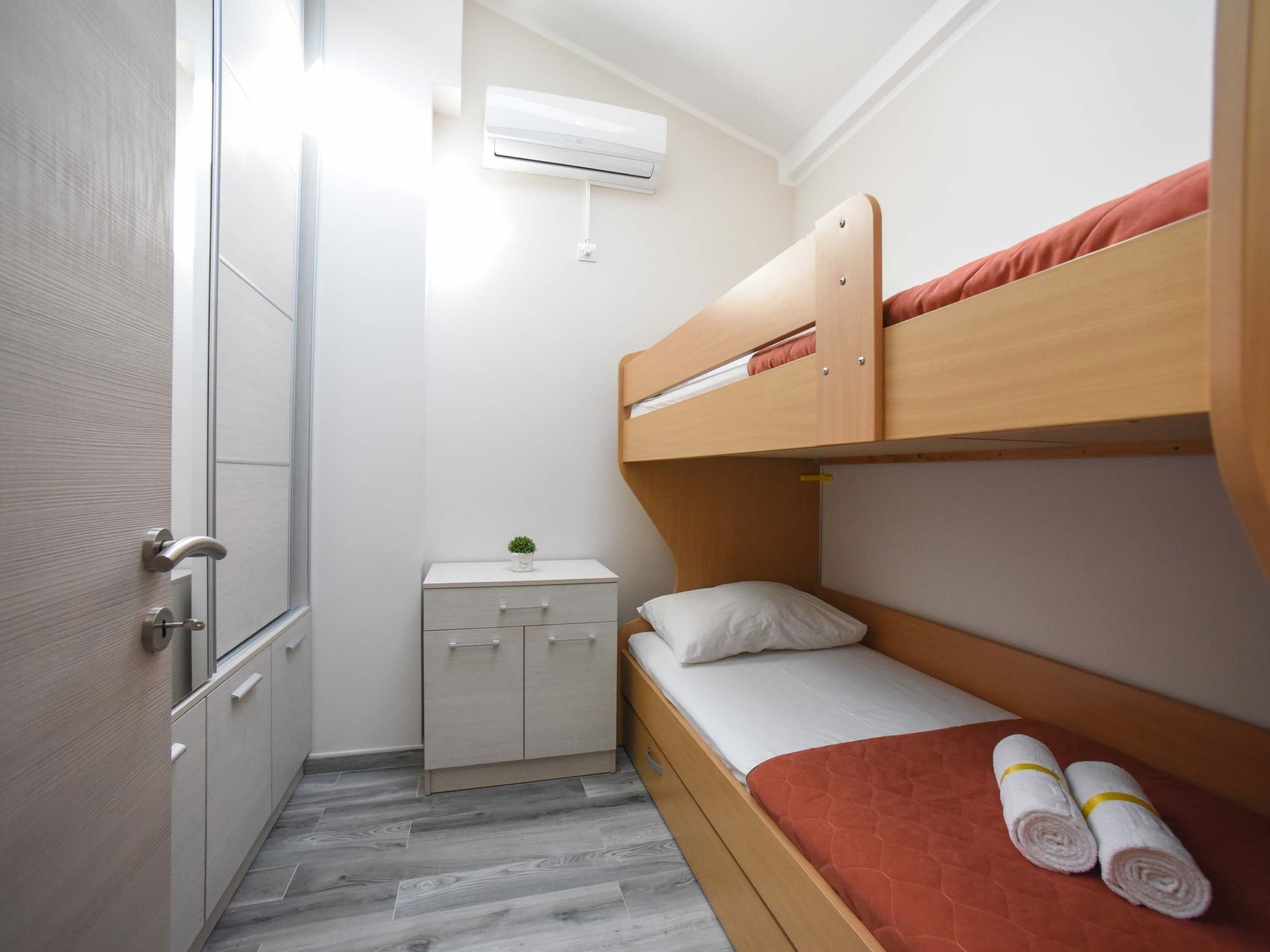 Een kleine kamer met een stapelbed, een klein nachtkastje met een plantje en een garderobe.
