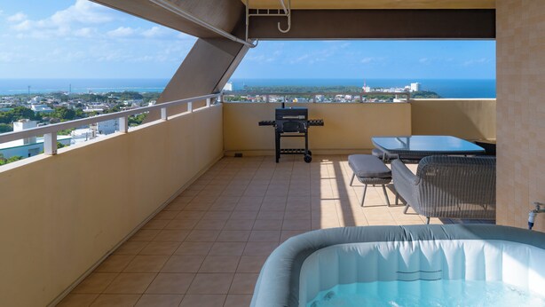 Un balcón con jacuzzi, mobiliario exterior y vistas a la ciudad y al océano.