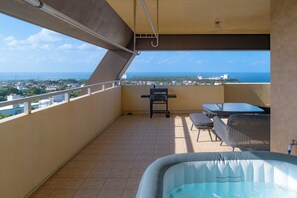 A balcony with a hot tub, outdoor furniture, and a view of the city and ocean. - Nayana Hills Top Sky View (Yomitan)