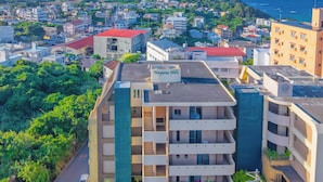 Un hotel moderno de gran altura con varios balcones, piscina en la azotea y vistas a la ciudad y al océano.