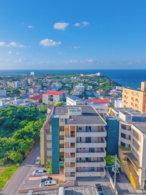 A high-rise hotel with multiple balconies, a rooftop pool, and a view of the city and ocean. - Nayana Hills Top Sky View (Yomitan)