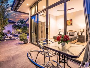 A hotel room with a glass door leading to a pool area, a bed with a nightstand, and a table with chairs. - "Villa Sabai" mit Terrasse by Interhome (Pattaya)