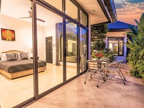 A modern bedroom with a bed, a glass door leading to a patio, and a dining area with a table and chairs. - "Villa Sabai" mit Terrasse by Interhome (Pattaya)