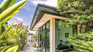 Una casa moderna con facciata in vetro, un patio con mobili da esterno e vegetazione lussureggiante.