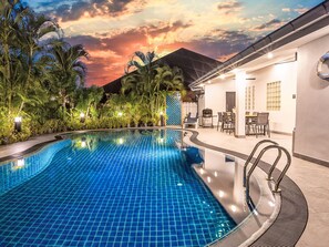 A swimming pool with a tiled edge, surrounded by palm trees and a building with a covered patio. - "Villa Sabai" mit Terrasse by Interhome (Pattaya)