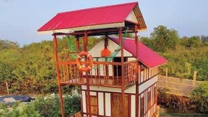 Een houten gebouw met twee verdiepingen en een rood dak, omringd door weelderige begroeiing.