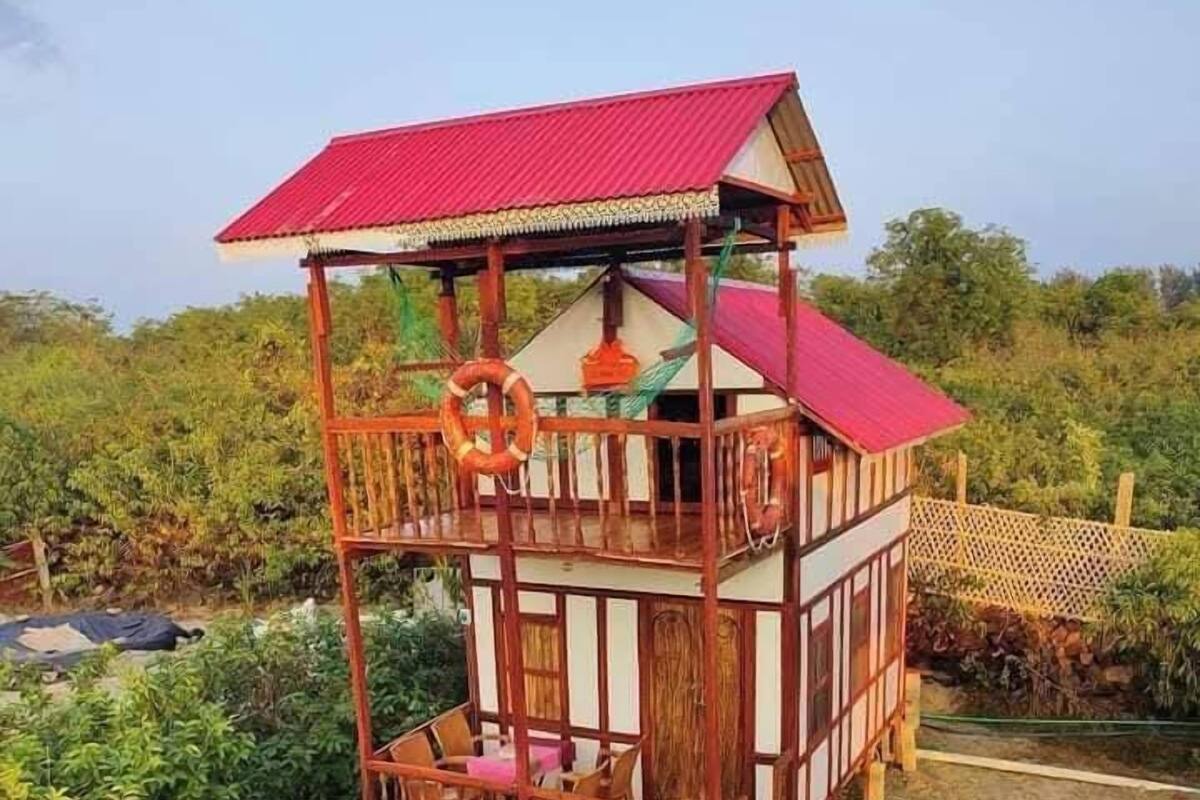 A two-story wooden structure with a red roof, surrounded by lush greenery.