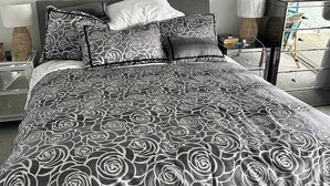 A neatly made bed with a black and white rose pattern bedspread, a bedside table with a lamp, and a large mirror on the wall. - Waterfront 3 bed Townhouse in gated community (Patterson Lakes)
