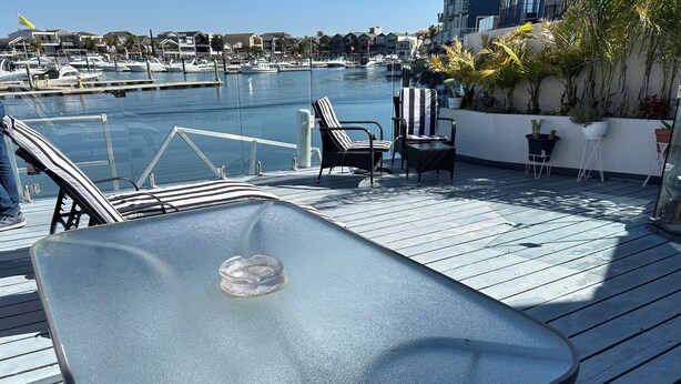 A deck with a glass-top table, chairs, and potted plants. - Waterfront 3 bed Townhouse in gated community (Patterson Lakes)